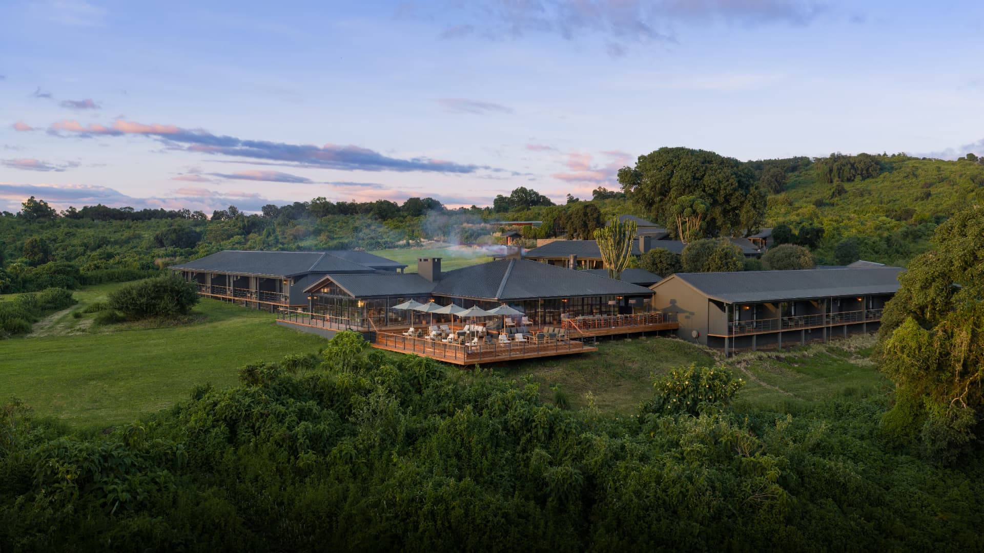 Aerial view of Laba Ngorongoro Lodge at dusk, with pitched roofs, a terrace of loungers and parasols above the highland forest