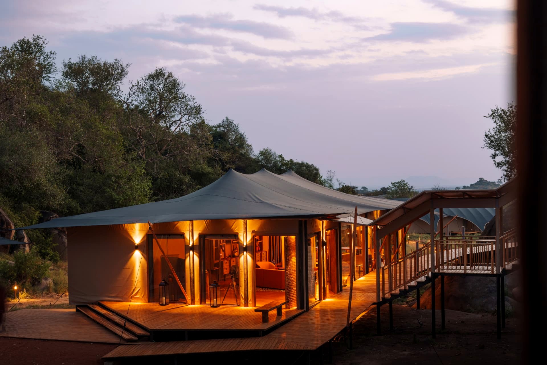 Warangi Ridge guest tent at dusk, lantern-lit canvas suite with wooden deck and open bush views in the Serengeti