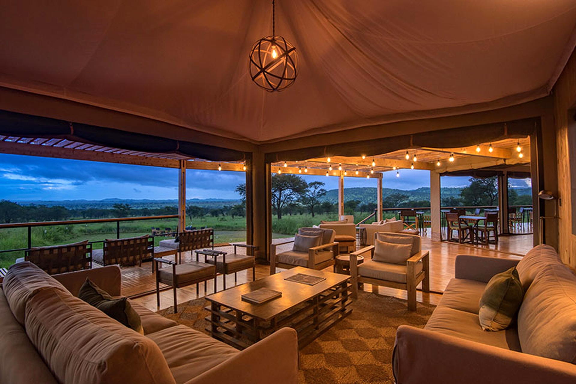 Dunia Camp lounge at dusk, canvas tent interior with sofas, lantern light and sweeping views of the Serengeti plains