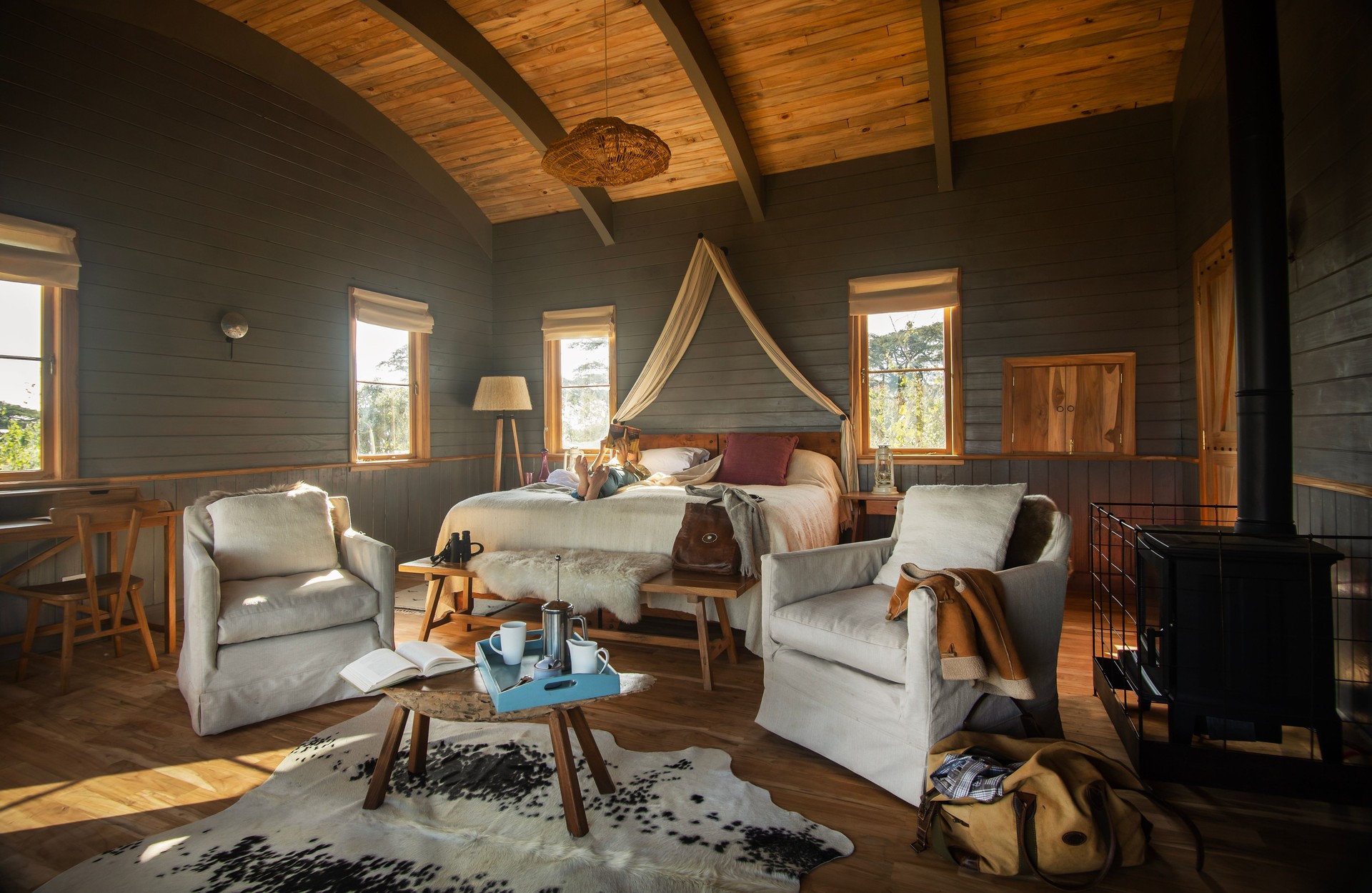 Entamanu Ngorongoro suite interior with vaulted timber ceiling, canopied bed, linen armchairs, wood stove and highland views