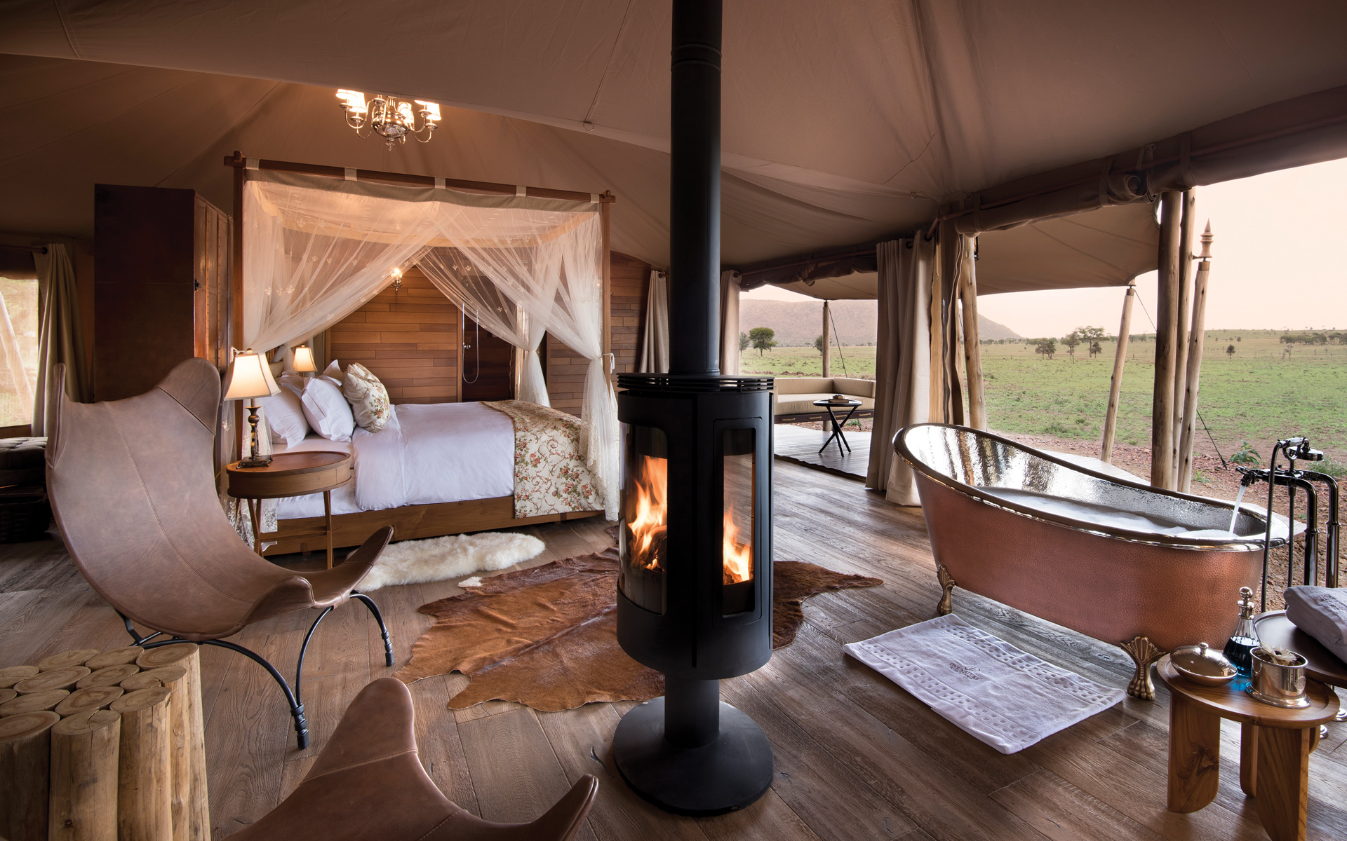One Nature Nyaruswiga luxury tent interior, four-poster bed, fireplace and copper bathtub with Serengeti views