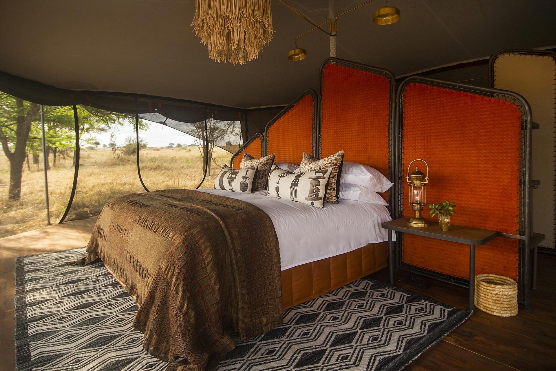 Closed while relocating: approx. Nov 8–Dec 14 and Apr 2–May 31. Siringit Migration Camp tent interior, king bed with orange woven screens, brass lantern and open views over the Serengeti grasslands