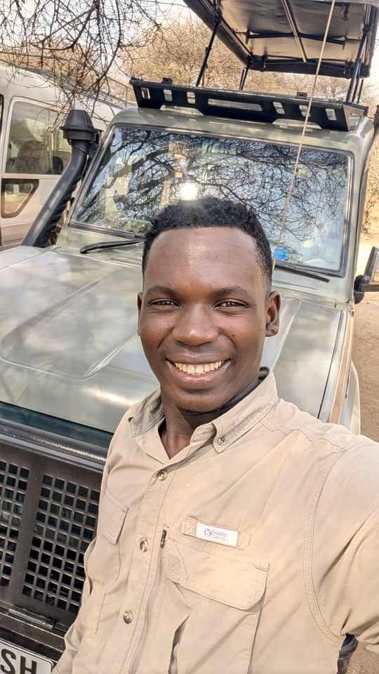 Hodari safari guide standing beside an olive green Toyota Land Cruiser safari station wagon with pop-up roof in the Serengeti