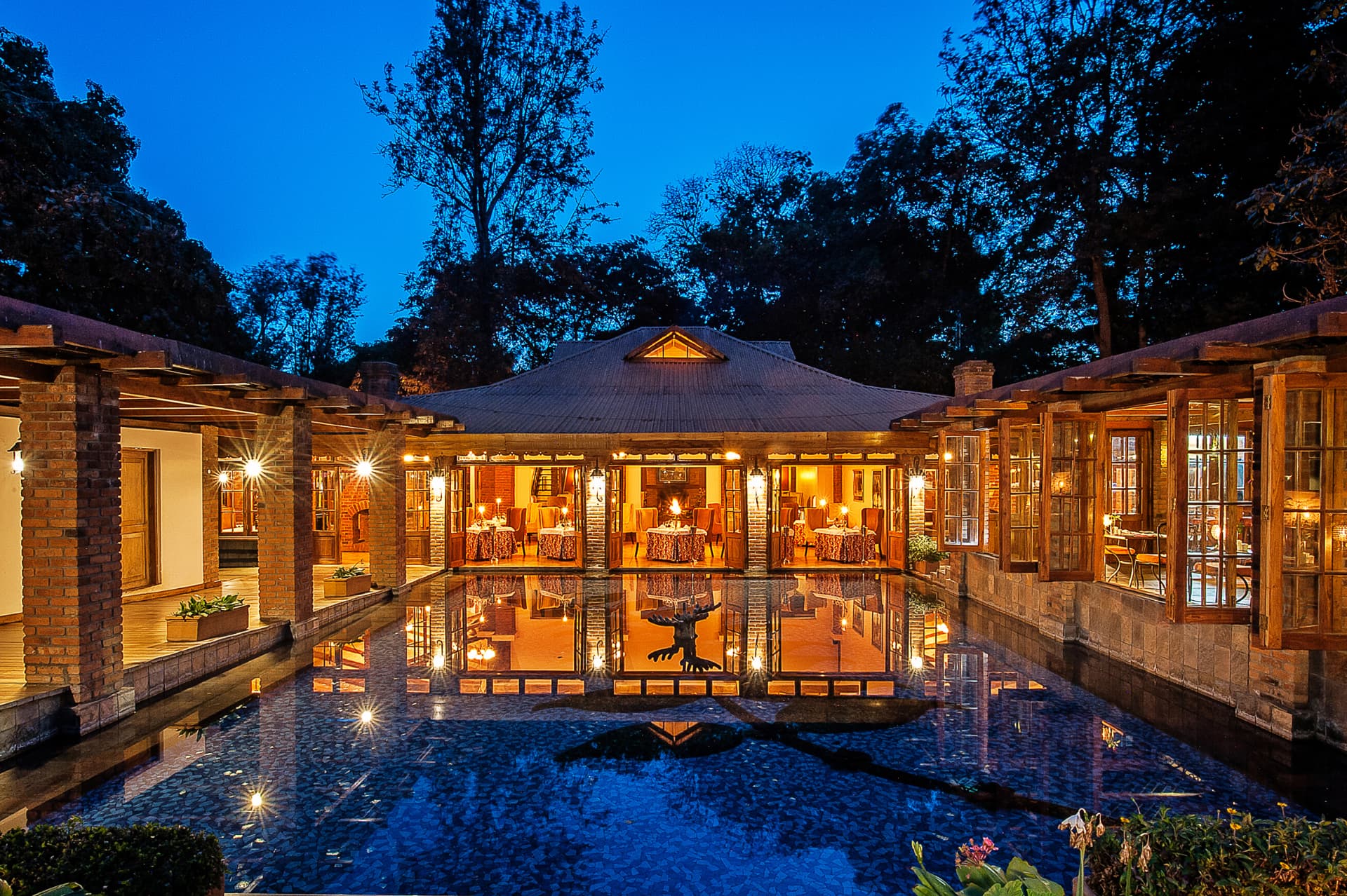 Arusha Coffee Lodge restaurant exterior at dusk, lantern-lit veranda reflected in the courtyard pool near Arusha, Tanzania