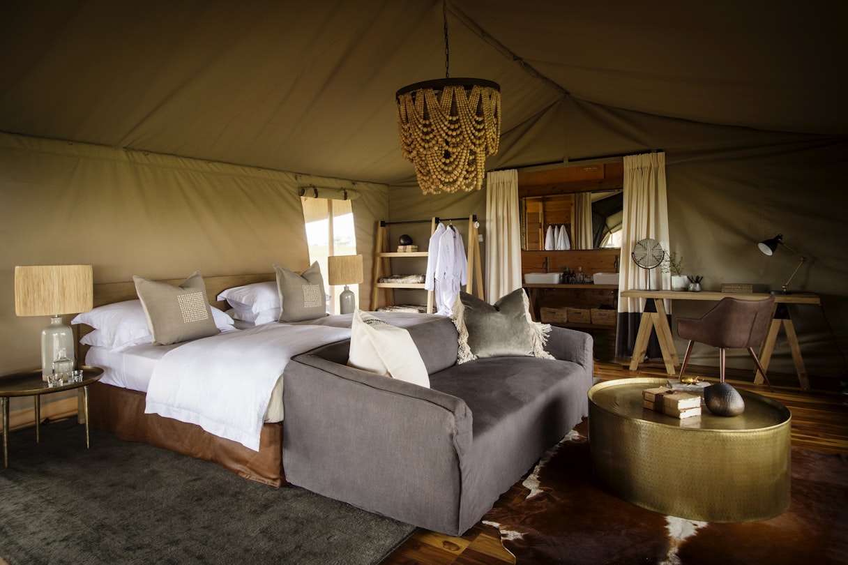 Siringit Serengeti Camp luxury tent interior, king bed, grey daybed, beaded chandelier and brass coffee table in the Central Serengeti