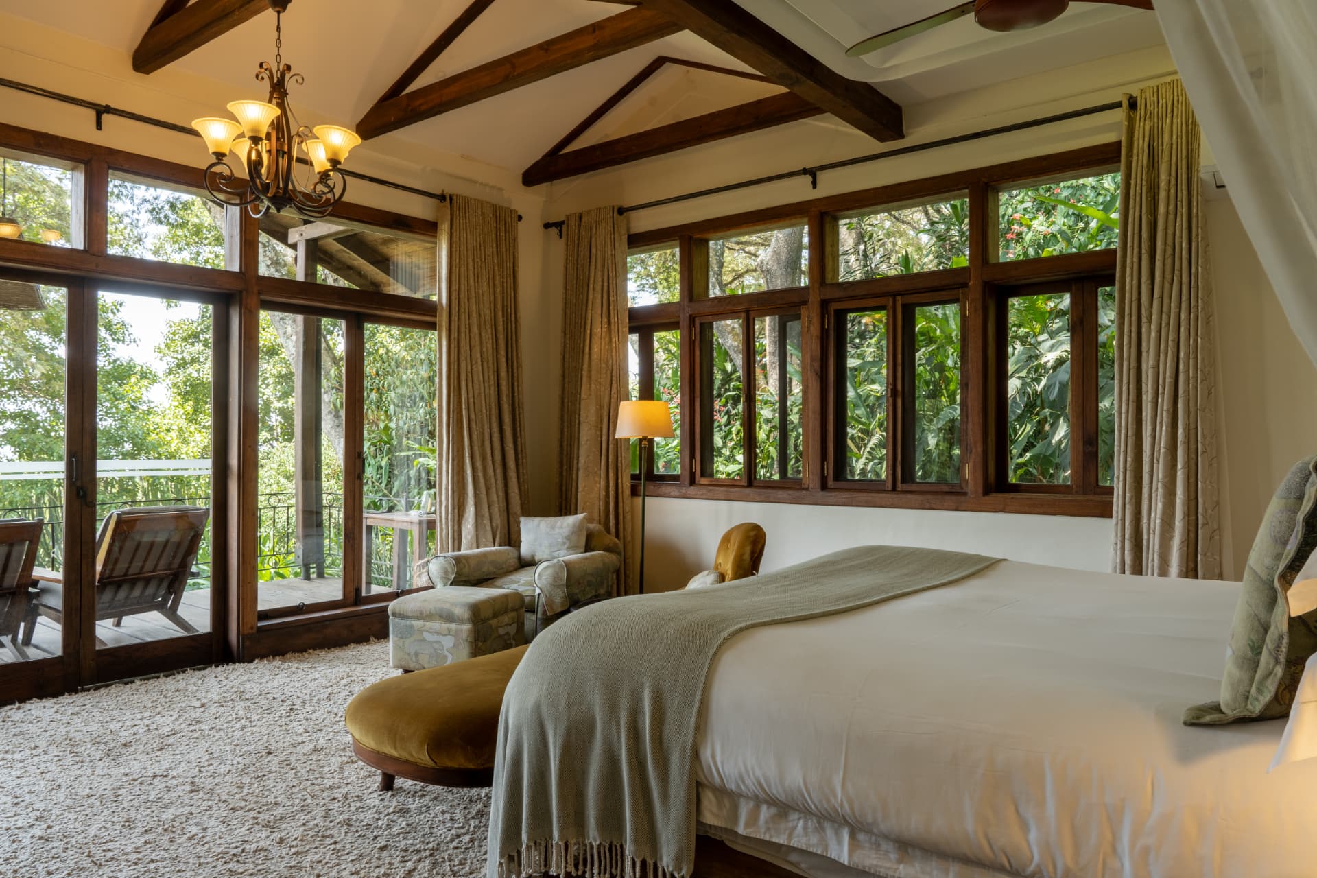 Gibb's Farm guest room with king bed, wooden beams, chandelier and garden doors opening to the Ngorongoro highlands forest