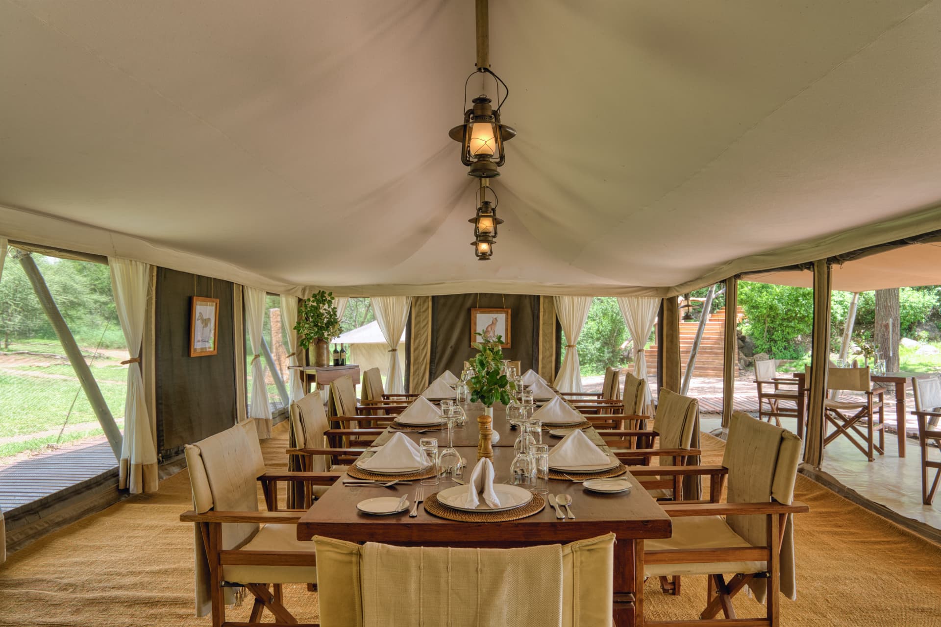 Serengeti Pioneer Camp dining tent interior, long wooden table set for dinner, hanging lanterns and open views over the Serengeti