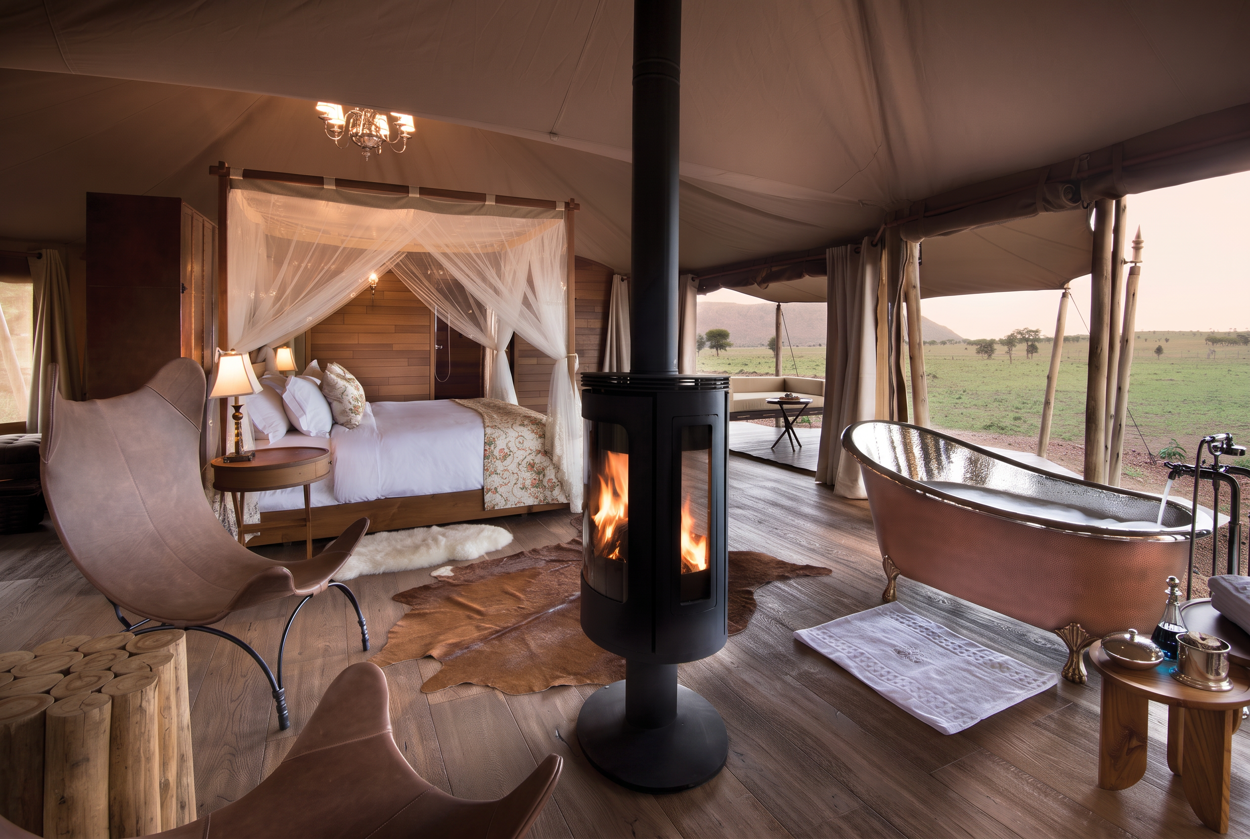 One Nature Nyaruswiga luxury tent interior, four-poster bed, fireplace and copper bathtub with Serengeti views